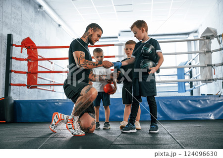 Preparing for the sparring. Young tattooed coach teaching the kids boxing techniques 124096630