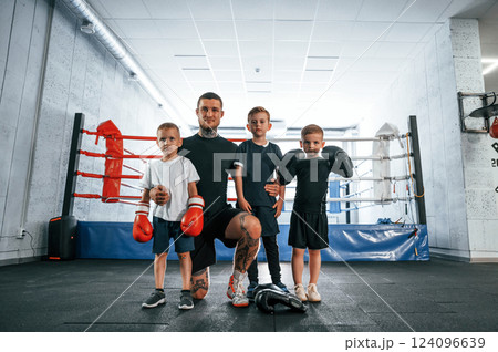 Posing for the camera together. Young tattooed coach teaching the kids boxing techniques 124096639