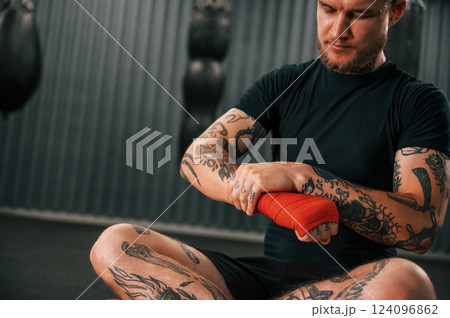 Almost ready. Wearing hand wraps. Young tattooed man is practicing boxing indoors in the gym Almost ready. Wearing hand wraps. Young tattooed man is practicing boxing indoors in the gym 124096862