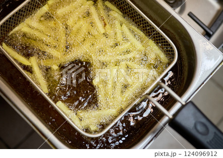 Freshly cut potato strips sizzle in bubbling oil, transforming into crispy golden fries. The bustling kitchen emits delicious aromas as they cook to perfection 124096912