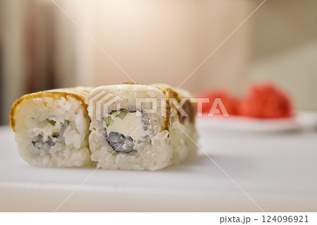 A close-up view of freshly made sushi rolls showcasing creamy filling and crispy edges. The setting features warm lighting with a plate of wasabi in the background A close-up view of freshly made sushi rolls showcasing creamy filling and crispy edges. The setting features warm lighting with a plate of wasabi in the background 124096921