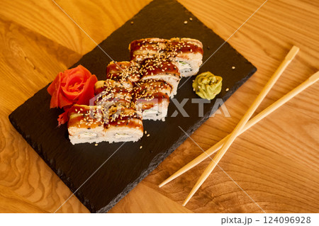 Sushi rolls are expertly arranged on a black slate plate, accompanied by ginger and wasabi. The warm wooden table creates a relaxing atmosphere during lunch or dinner Sushi rolls are expertly arranged on a black slate plate, accompanied by ginger and wasabi. The warm wooden table creates a relaxing atmosphere during lunch or dinner 124096928