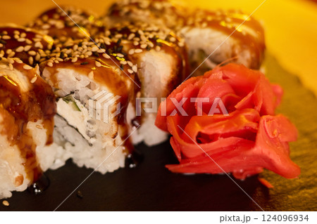 Sushi rolls topped with a glossy sauce and sesame seeds are placed next to vibrant pickled ginger. The dim lighting adds a warm atmosphere to the restaurant experience Sushi rolls topped with a glossy sauce and sesame seeds are placed next to vibrant pickled ginger. The dim lighting adds a warm atmosphere to the restaurant experience 124096934