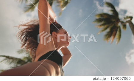 Young woman peacefully relaxing on a tropical beach. Feeling the warm sun and gentle wind. Carefree and happy in a vibrant blue sky with swaying palm trees Young woman peacefully relaxing on a tropical beach. Feeling the warm sun and gentle wind. Carefree and happy in a vibrant blue sky with swaying palm trees 124097060