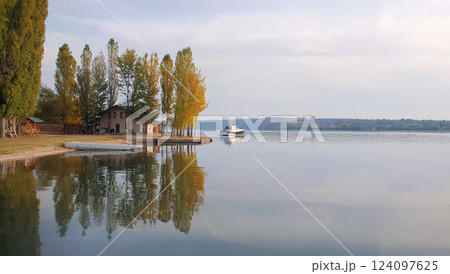 Scenic view with a house on the riverbank of Nistru river and a yacht floating. Autumn season landscape, colorful trees and beautiful sky reflected on the water surface 124097625