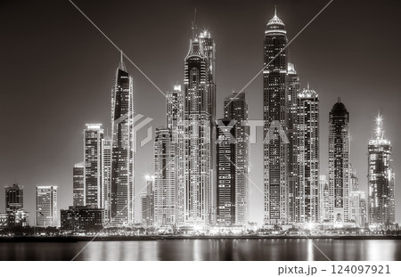 Urban city skyline with illuminated skyscrapers and waterfront railing in black and white at night, Dubai Marina bay UAE 124097921
