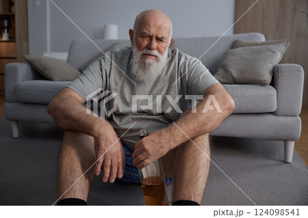 Depressed senior man drinking alcohol alone sitting on floor at home 124098541