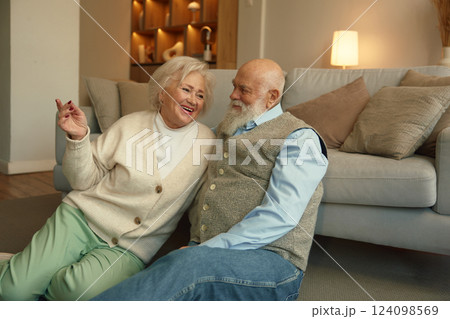 Happy carefree elderly couple talking and sitting on floor in home living room 124098569