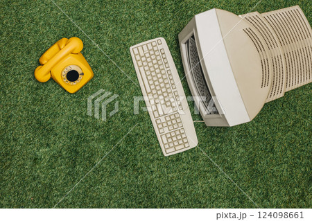 Vintage PC and yellow dial phone on green grass, top view. Monitor and keyboard as in 90s Vintage PC and yellow dial phone on green grass, top view. Monitor and keyboard as in 90s 124098661