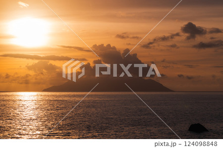 Golden sunset casting a serene glow over a calm sea with an island Golden sunset casting a serene glow over a calm sea with an island 124098848