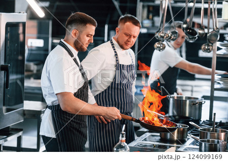 Flaming the meal on frying pan. Kitchen workers is together preparing the food 124099169