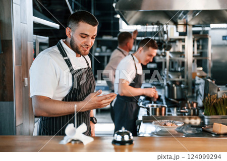 Standing near the table with bell. Kitchen workers is together preparing the food Standing near the table with bell. Kitchen workers is together preparing the food 124099294