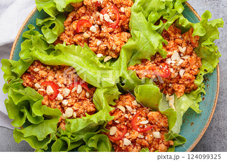 Close up of lettuce wraps filled with minced meat and topped with peanuts and chili pepper flakes on a plate, healthy protein dish Close up of lettuce wraps filled with minced meat and topped with peanuts and chili pepper flakes on a plate, healthy protein dish 124099325