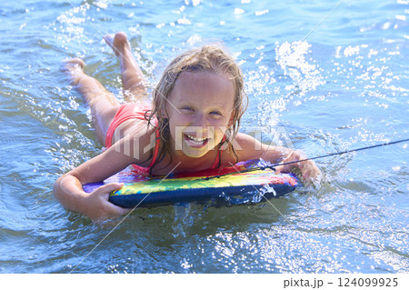 A little girl is having fun on the beach, swimming on a board A little girl is having fun on the beach, swimming on a board 124099925