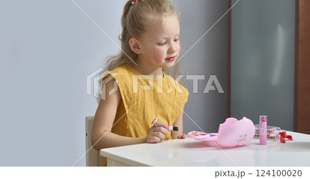 A little girl paints her cheeks with baby blush. The child draws with children's cosmetics. A daughter imitates her mother. A little girl paints her cheeks with baby blush. The child draws with children's cosmetics. A daughter imitates her mother. 124100020