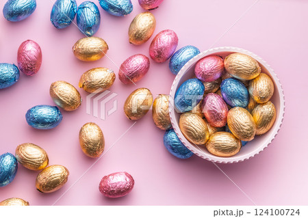 Chocolate easter eggs wrapped in multi colored foil in bowl on pink background. Top view. 124100724