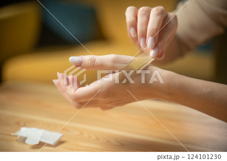 Applying a Band-Aid to treat a small cut on the arm while sitting at a wooden table Applying a Band-Aid to treat a small cut on the arm while sitting at a wooden table 124101230