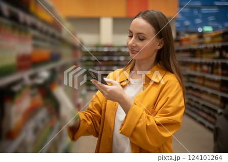 Woman scans juice in supermarket aisle while shopping for healthy beverages during afternoon Woman scans juice in supermarket aisle while shopping for healthy beverages during afternoon 124101264