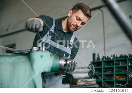 Working with metal. Man in uniform is indoors developing details of agriculture technique 124101652