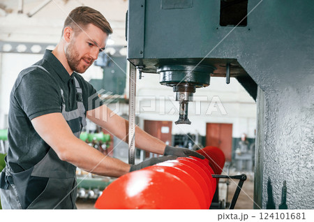Measuring red colored sharp part. Man in uniform is in workstation developing details of agriculture technique Measuring red colored sharp part. Man in uniform is in workstation developing details of agriculture technique 124101681