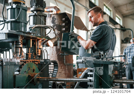 Standing by metal processing device. Man in uniform is in workstation developing details of agriculture technique Standing by metal processing device. Man in uniform is in workstation developing details of agriculture technique 124101704