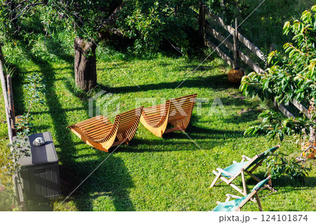 Above view wooden loungers rest under shady tree lush green lawn eco fresh open-air comfort. Relaxing backyard scene invites peaceful summer retreat orchard fence framing scenic hillside view 124101874