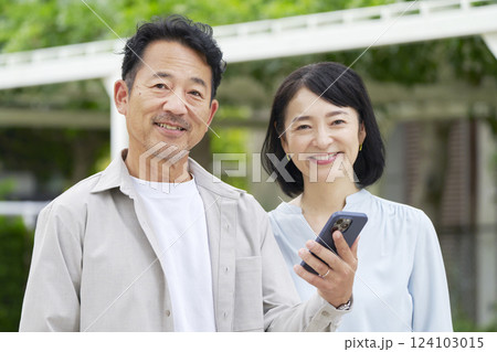 中年の夫婦 スマートフォンを持つ 屋外 中年の夫婦 スマートフォンを持つ 屋外 124103015
