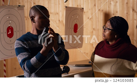 Shooting gallery worker meeting with customers, greeting them, demonstrating how to safely reload pistol. Firing range expert welcoming clients, doing hand shake, teaching weapon handling, camera B 124103085