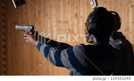 Man holds pistol, enjoying recreational shooting experience in firing range next to instructor reloading weapons. Employee loading firearms for shooting range company customers, camera B Man holds pistol, enjoying recreational shooting experience in firing range next to instructor reloading weapons. Employee loading firearms for shooting range company customers, camera B 124103249