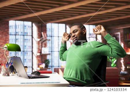 Person in home office stretching back after sitting at desk too long. Freelancer in living room doing muscle exercises to relieve backache pain gained from incorrect posture Person in home office stretching back after sitting at desk too long. Freelancer in living room doing muscle exercises to relieve backache pain gained from incorrect posture 124103334