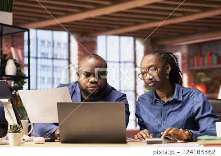 African American couple reviews their taxes and finances at home, using a calculator and laptop to track expenses, manage bills and plan their budget at home office. Financial responsibility. 124103362
