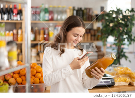 European teen girl customer at shop scans QR code on peach juice bottle using phone camera European teen girl customer at shop scans QR code on peach juice bottle using phone camera 124106157