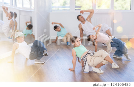 Young girl and group of children in casual wear training hip hop movements on floor in dance class with male coach 124106486
