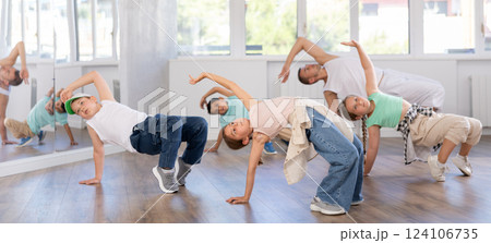 Dynamic young girl sitting in breakdance pose in dance studio with other teenage dancers 124106735
