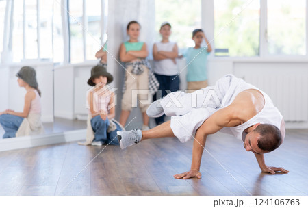 Young male coach demonstrating to group of teen children hip hop dance moves in class Young male coach demonstrating to group of teen children hip hop dance moves in class 124106763