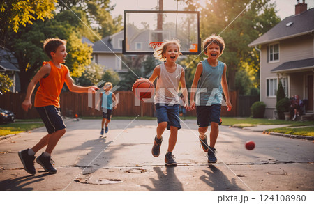 Group of young boys playing basketball in a driveway. One of the boys is holding a basketball and running towards the hoop 124108980
