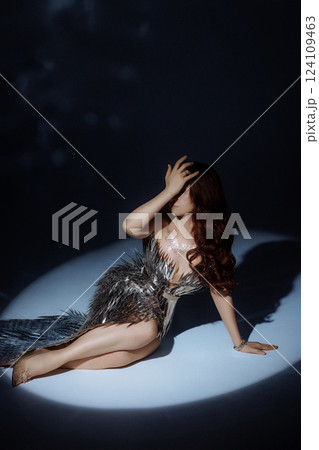 A woman in a metallic gown poses under a focused light. A woman in a metallic gown poses under a focused light. 124109463