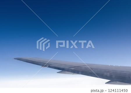 A stunning airplane wing gliding above clouds in a clear blue sky, embodying adventure and freedom. Blue and white sky background under the wing of an airplane. The concept of travel. A stunning airplane wing gliding above clouds in a clear blue sky, embodying adventure and freedom. Blue and white sky background under the wing of an airplane. The concept of travel. 124111450
