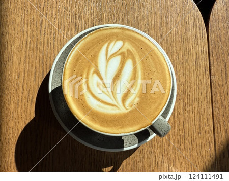 cup of coffee flower drawing on wooden table Close up cup of cappuccino on saucer. Top view of a drawing of a heart on coffee foam. Morning coffee stands on a wooden brown table. copy place 124111491