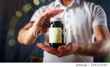 Hands holding a supplement bottle for energy with an empty label space for text. 124113515