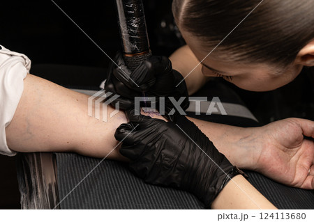 female tattoo artist applies a tattoo to a woman arm. She outlines tattoo female tattoo artist applies a tattoo to a woman arm. She outlines tattoo 124113680