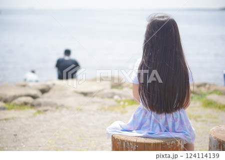 海辺から岩に座って海を眺めている小学生の女の子の後ろ姿 124114139