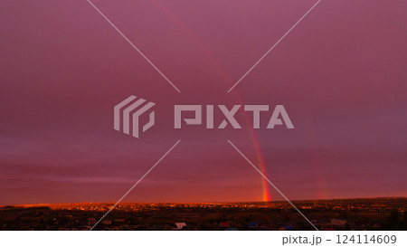 Faint rainbow arching across dramatic sunset sky over rooftops. 124114609