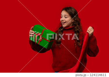 Excited girl holds Christmas gift and Santa hat. Excited girl holds Christmas gift and Santa hat. 124114611