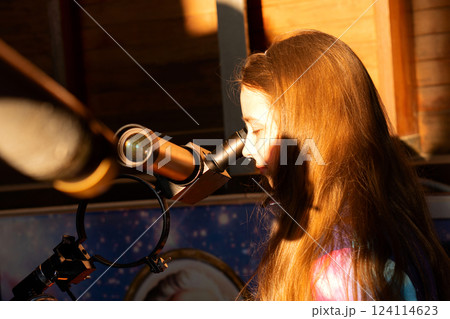 Side view of young girl looking through solar telescope. 124114623