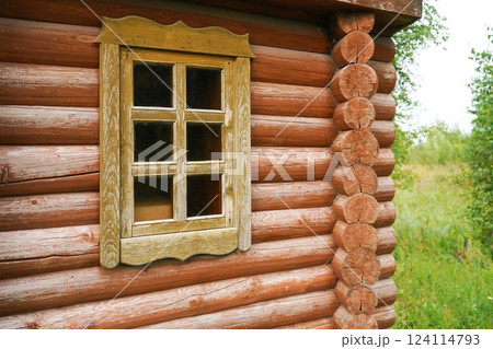 Window with a wooden frame in a wooden house and a tree branch in the foreground 124114793