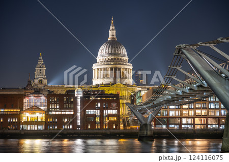 Pedestrians walk along the Millennium Bridge at night, with St. Paul's Cathedral illuminated in the background, creating a captivating urban scene over the River Thames in London. Pedestrians walk along the Millennium Bridge at night, with St. Paul's Cathedral illuminated in the background, creating a captivating urban scene over the River Thames in London. 124116075