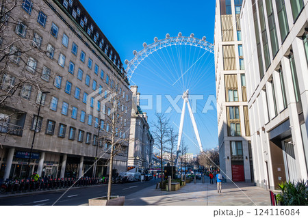A clear blue sky provides a stunning backdrop to the London Eye towering over the street. Visitors stroll by modern buildings, enjoying the lively atmosphere of the city. A clear blue sky provides a stunning backdrop to the London Eye towering over the street. Visitors stroll by modern buildings, enjoying the lively atmosphere of the city. 124116084