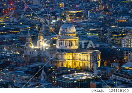 St Paul's Cathedral stands illuminated against the London skyline during evening hours. Surrounding buildings reflect city lights, showcasing a vibrant urban atmosphere. 124116100