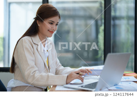 professional businesswoman planning and analyzing marketing charts and financial documents with a laptop and calculator papers on the desk 124117644